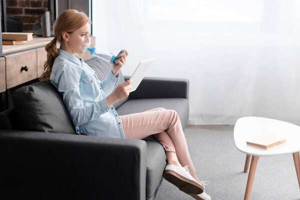 side view of asthmatic woman using inhaler with spacer and holding digital tablet 