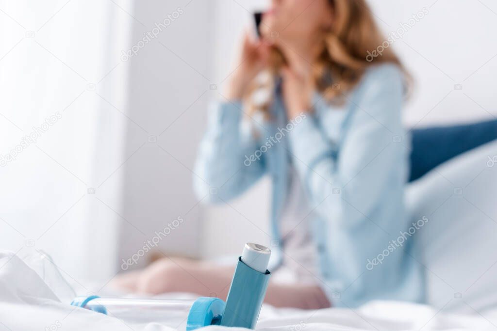 selective focus of inhaler with spacer on bed near sick woman 