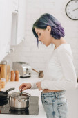 Dívka s barevnými vlasy připravuje jídlo a dotýká pan víko v blízkosti kuchyně sporák