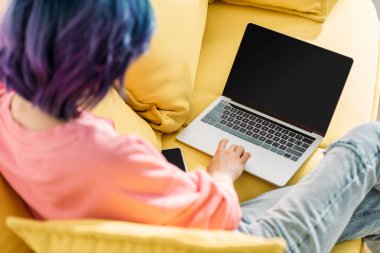 Selective focus of freelancer with colorful hair and laptop sitting on sofa clipart