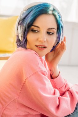 Beautiful woman with colorful hair and headphones listening music and looking away clipart