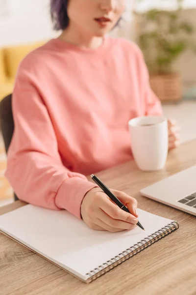 Vista Cortada Freelancer Segurando Xícara Chá Escrevendo Caderno Mesa — Fotografia de Stock