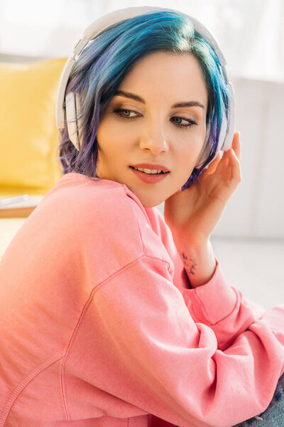 Beautiful woman with colorful hair and headphones listening music and looking away