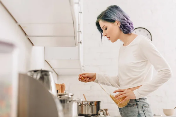 Selective focus of girl with colorful hair putting pasta in pan near kitchen stove — Stock Image Selective Focus Girl Colorful Hair Putting Pasta Pan Kitchen Stove Stock Photo