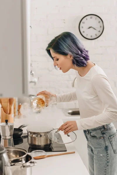 Selective focus of girl with colorful hair putting pasta in pan with steam near kitchen stove — Stock Image Selective Focus Girl Colorful Hair Putting Pasta Pan Steam Kitchen Stock Photo