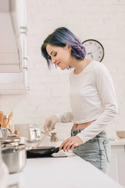 Selective focus of girl with colorful hair preparing food with spatula on frying pan in kitchen — Stock Image Selective Focus Girl Colorful Hair Preparing Food Spatula Frying Pan Royalty Free Stock Photos