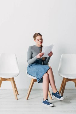 Attractive young woman reading resume while waiting for job interview  clipart