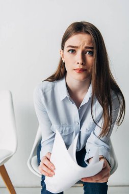 Selective focus of stressed candidate with resume looking at camera in office  clipart