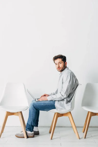 手持笔记本电脑坐在椅子上等待求职面试的男性侧视图 — 图库照片