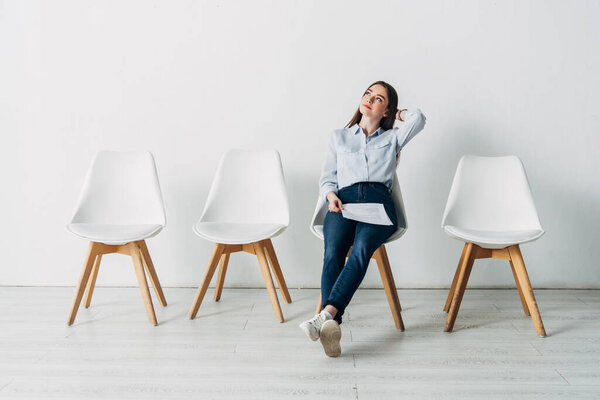 Dreamy applicant with resume sitting on chair in office 