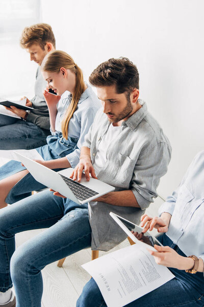 Работник, использующий ноутбук рядом с кандидатами с резюме
 