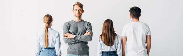 Панорамный снимок красивого мужчины со скрещенными руками, смотрящего в камеру рядом с сотрудниками офиса
 