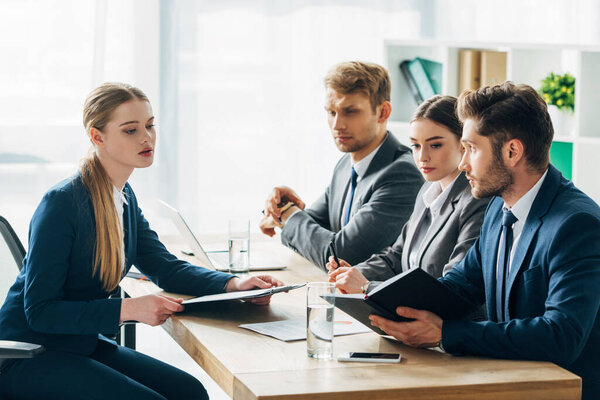 Side view of recruiters looking at employee with clipboard during job interview 