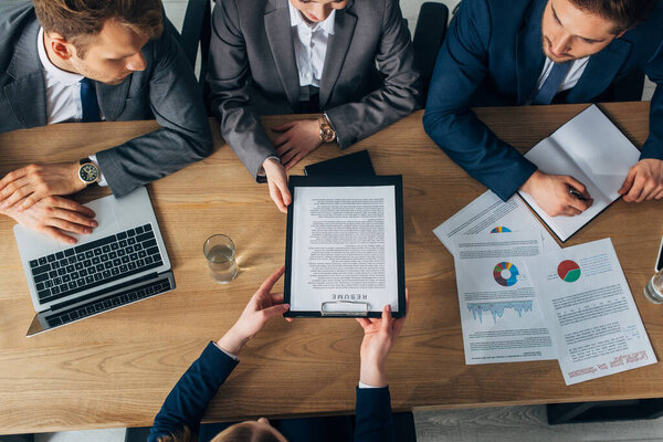 Overhead view of employee holding resume near recruiters at table 