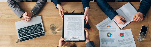 Overhead view of employee holding resume near recruiters at table, panoramic shot