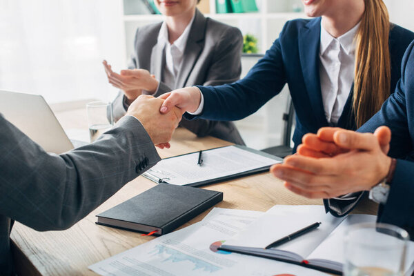 Cropped view of employee shaking hands with recruiter near colleagues during job interview 