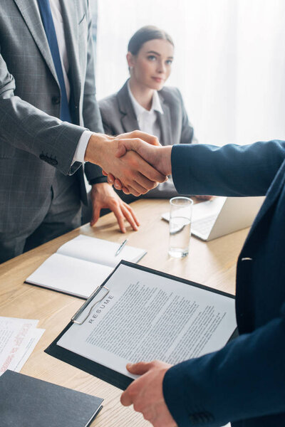 Selective focus of employee with resume shaking hands with recruiter in office 