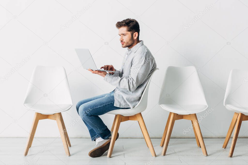 Side view of employee using laptop on chair in office 