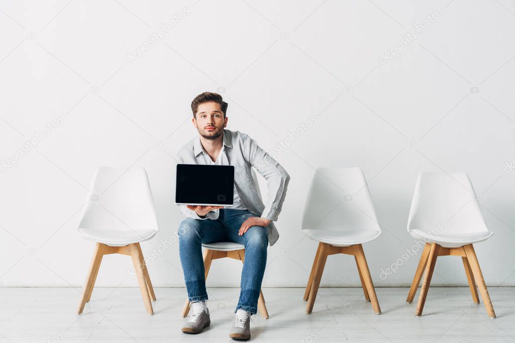 Handsome employee holding laptop with blank screen and looking at camera 