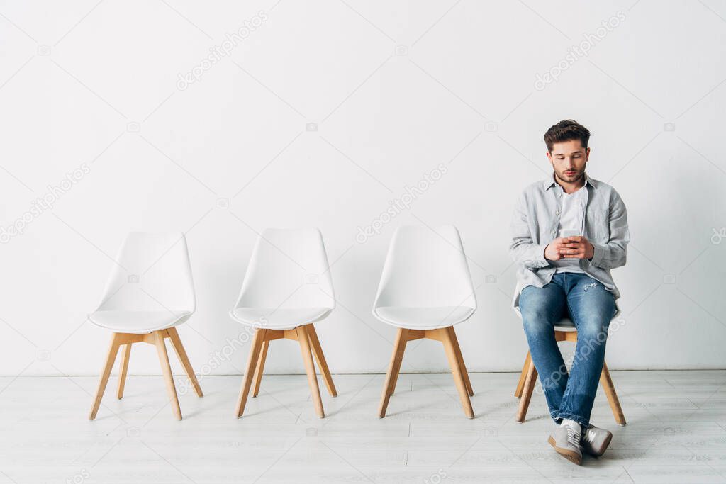 Handsome employee using smartphone while sitting on chair in office 