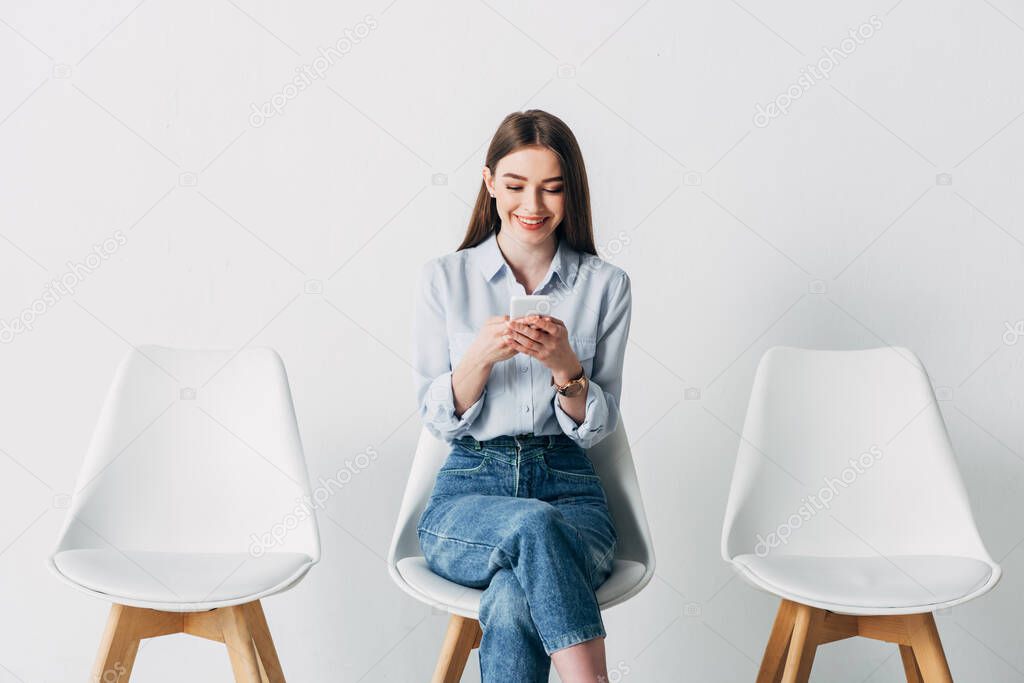 Smiling employee using smartphone while waiting for job interview in office 