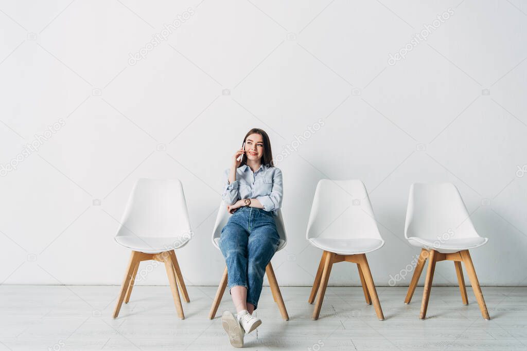 Beautiful smiling applicant talking on smartphone while sitting on chair in office 