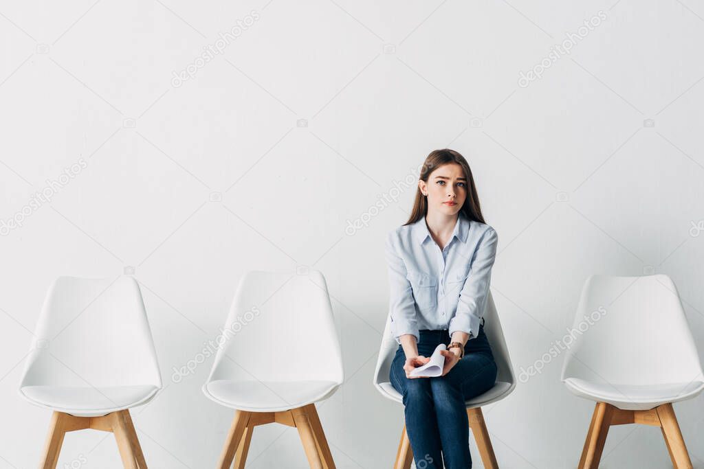 Attractive young woman holding resume and looking at camera in office 