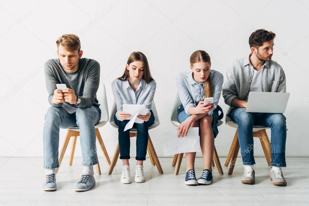 Employees using digital devices while sitting on chairs in office 
