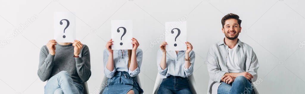 Panoramic shot of smiling man looking at camera near employees holding cards with question marks