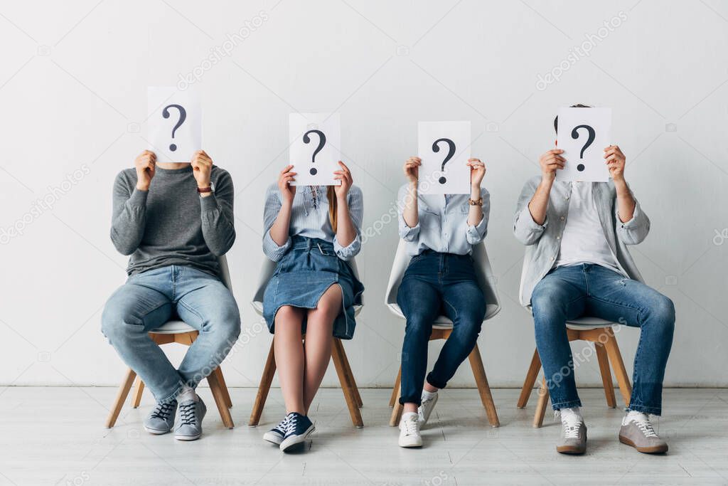 Young people holding cards with question marks while waiting for job interview in office 