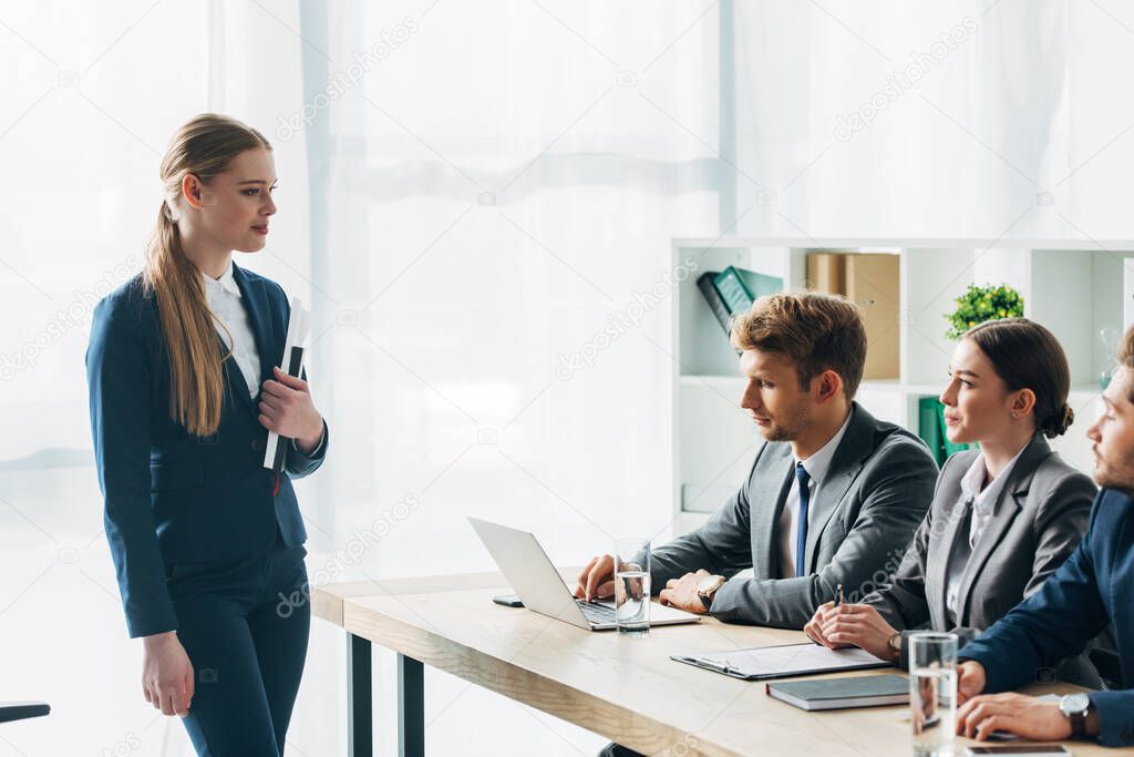 Selective focus of employee looking at recruiters with clipboard and laptop on table 