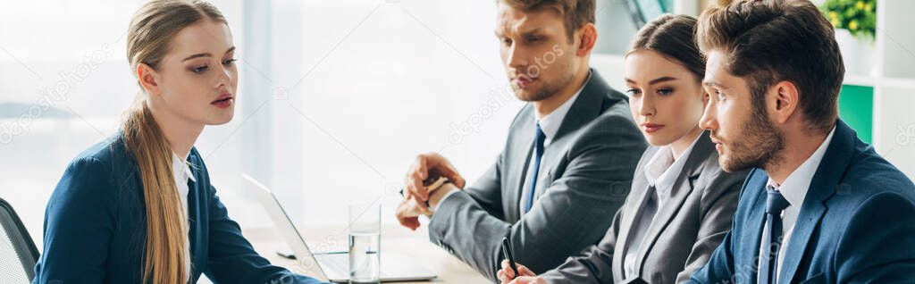 Panoramic shot of employee sitting at table near recruiters in office 
