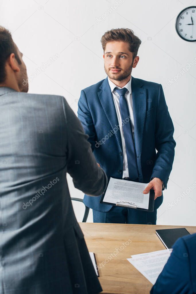 Selective focus of recruiter with clipboard shaking hands with employee in office 