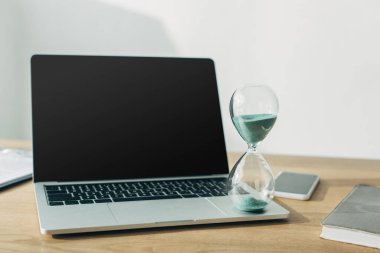 Bilgisayarda kum saati, akıllı telefonun yanında boş ekran ve ofisteki masanın üstünde defter. 