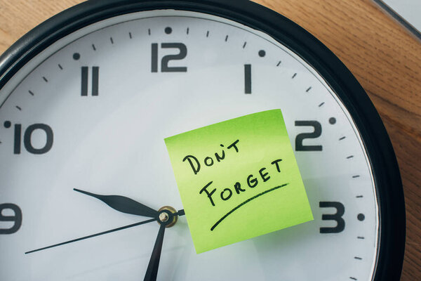 Top view of sticky note with dont forget lettering on clock on table