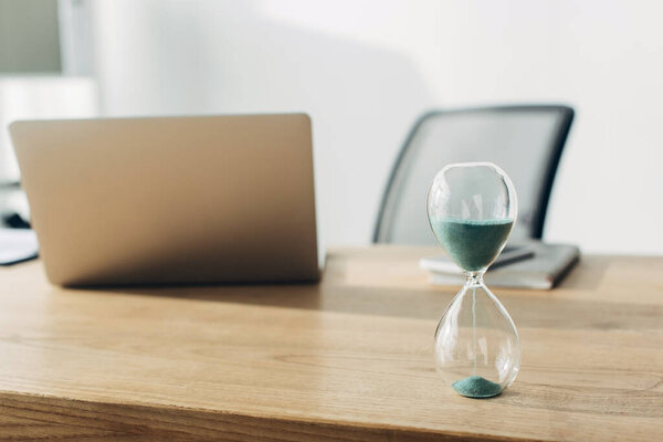 Selective focus of hourglass on table near laptop in office 