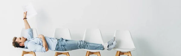 Panoramic shot of employee holding resume while lying on chairs in office