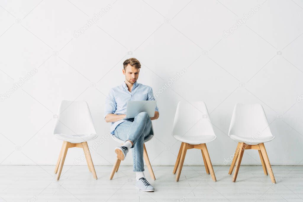 Handsome employee using laptop on chair in office 