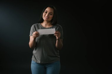 Siyah arka planda boş kart tutan pozitif artı büyük kızın ön görünümü