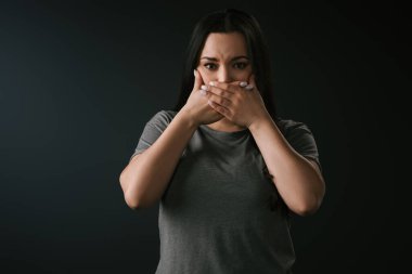 Güzel ve iri yarı bir kızın, elleri siyah arka planda, ağzını kapatarak sessizliğini bozması ön planda. 