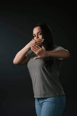 Plus size girl expressing silence with stop gesture isolated on black clipart