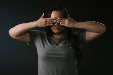 Siyah arka planda elleri olan gözleri örterek körlük yapan iri yarı bir kızın ön görüntüsü. 