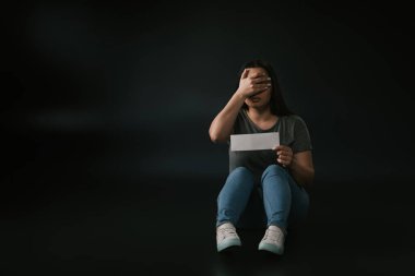 Front view of plus size girl with facepalm gesture and empty card in hand on black background clipart