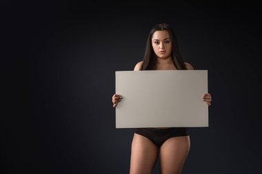 Siyah arka planda boş tahtası olan ciddi ve iri yarı bir kızın ön görüntüsü