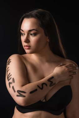 Siyah sutyenli büyük boy modelin portresi. Siyah vücutta izole edilmiş feminizm harfi var.