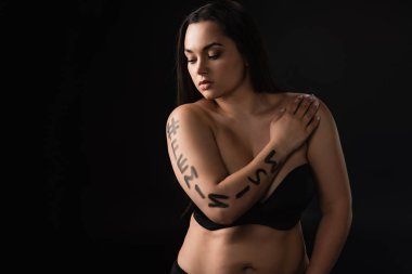 Vücudunda feminizm yazan büyük boy modelin ön görüntüsü. Göğsü kaplayan ve elleri siyah üzerine izole edilmiş.