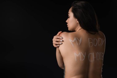 Back view of beautiful plus size model with lettering My Body My Choice on naked back isolated on black  clipart