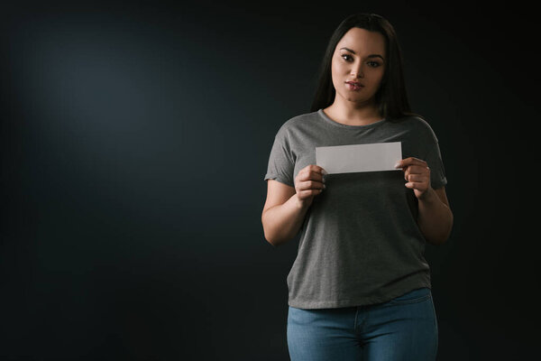 Вид спереди привлекательной девушки с пустой карточкой на чёрном фоне
