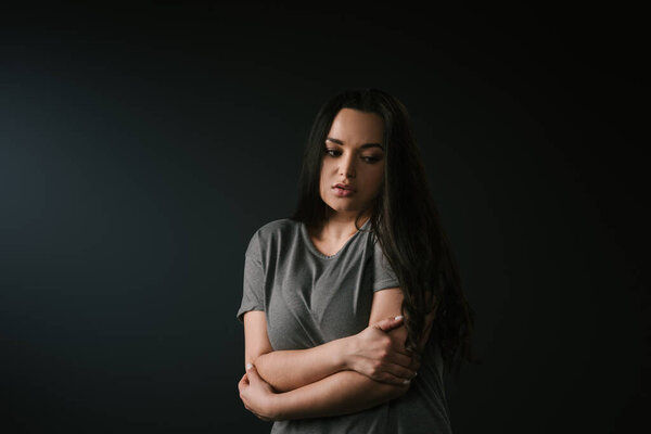 Грустный плюс размер девушка обнимает себя на черном фоне
 