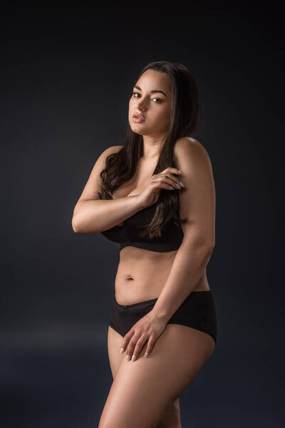 Plus size girl in underwear covering body with hands on black background